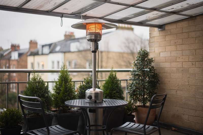 Una stufa elettrica compatta montata su un piccolo balcone coperto con persona seduta su una sedia davanti che gode del calore.