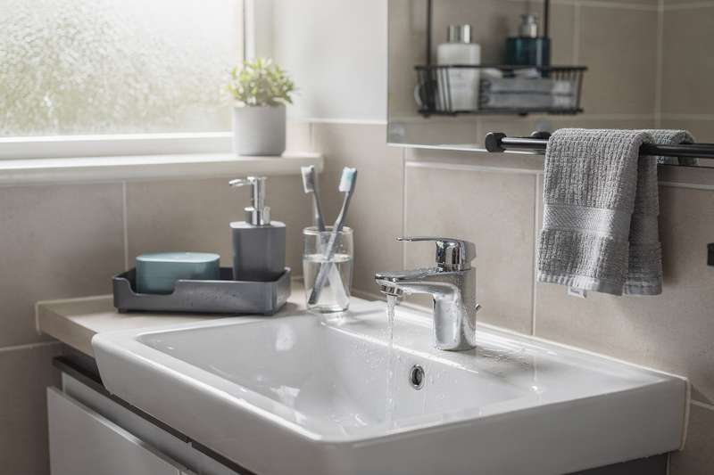 Mani che organizzano accessori da bagno moderni su uno scaffale in ceramica bianca.