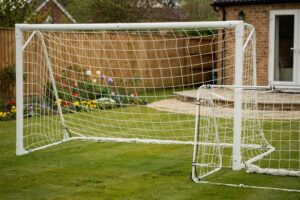 Persona che installa una porta da calcio pieghevole nel prato del giardino durante una giornata di sole.