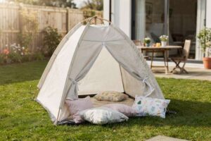 Bambina che gioca dentro una tenda a forma di tipi con cuscini colorati in salotto.