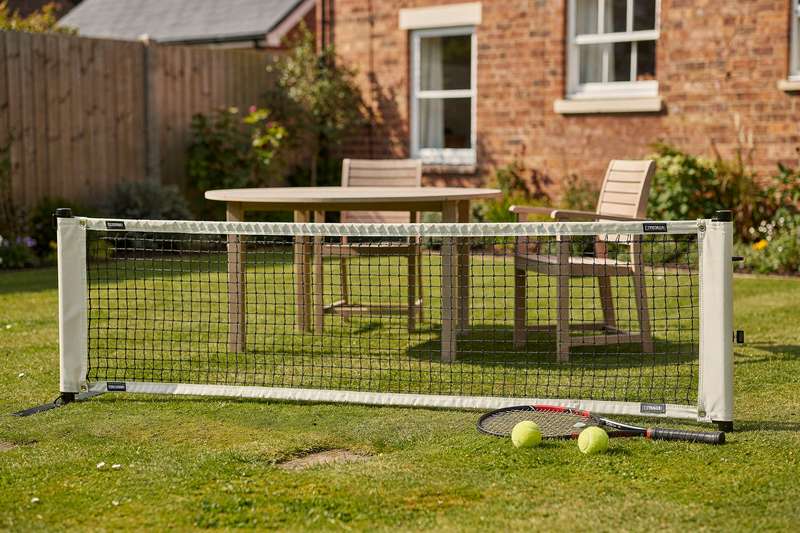 Una ragazza pratica il servizio con una racchetta davanti a una rete da tennis portatile in giardino.