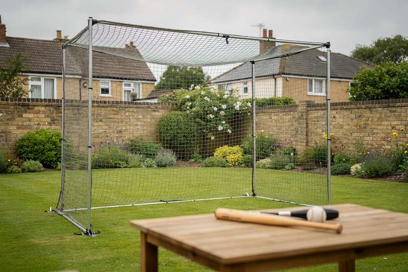 Persona che pratica swing di baseball all'interno di una gabbia da battuta installata in un giardino durante l'allenamento.